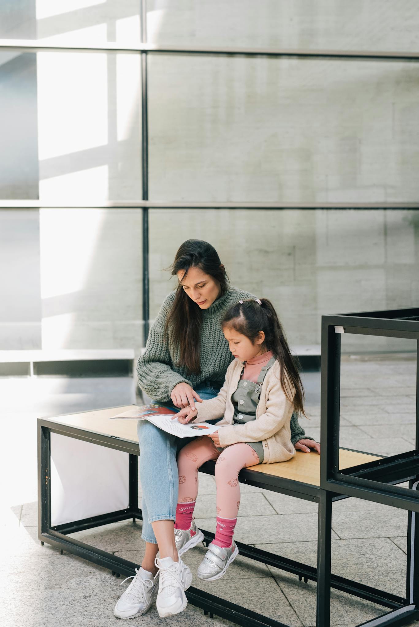 A mother and daughter enjoy reading together on a bench indoors, showcasing family bonding and education.